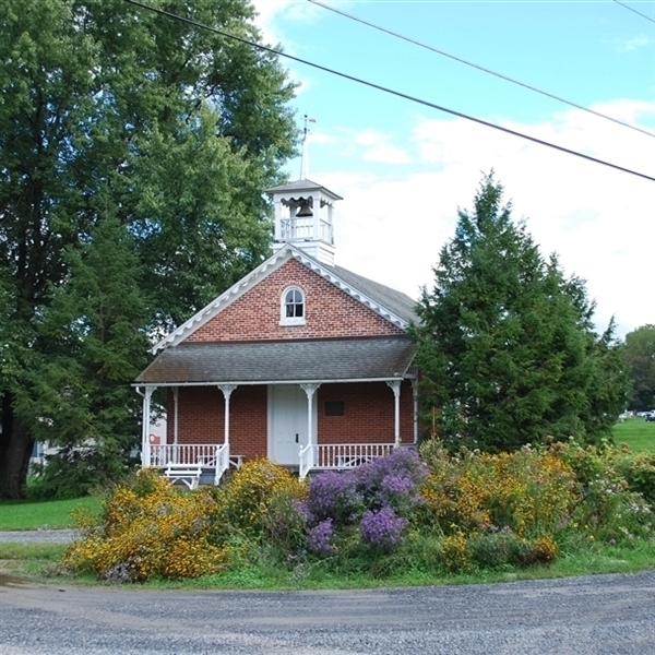 Image of the brick one-room schoolhouse with flowers in the foreground.