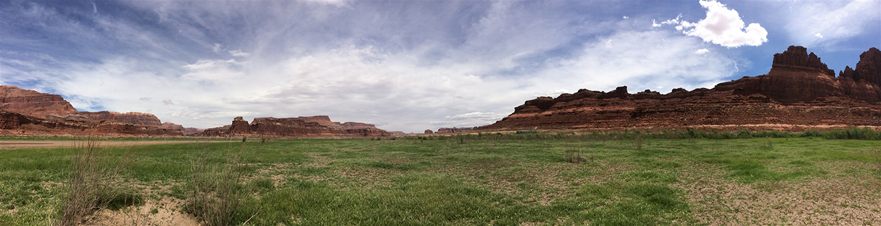 Panoramic view of mud gas sampling site; a large field with tall, flat cliffsides in the background 