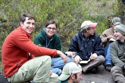 Small group of geology students sitting in a circle on the ground and smiling at the camera