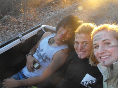 Three club members smiling with their arms around each other in the back of a pickup truck