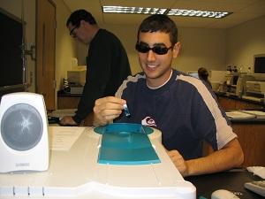 Smiling student places a slide into the viewing plate of a microscope