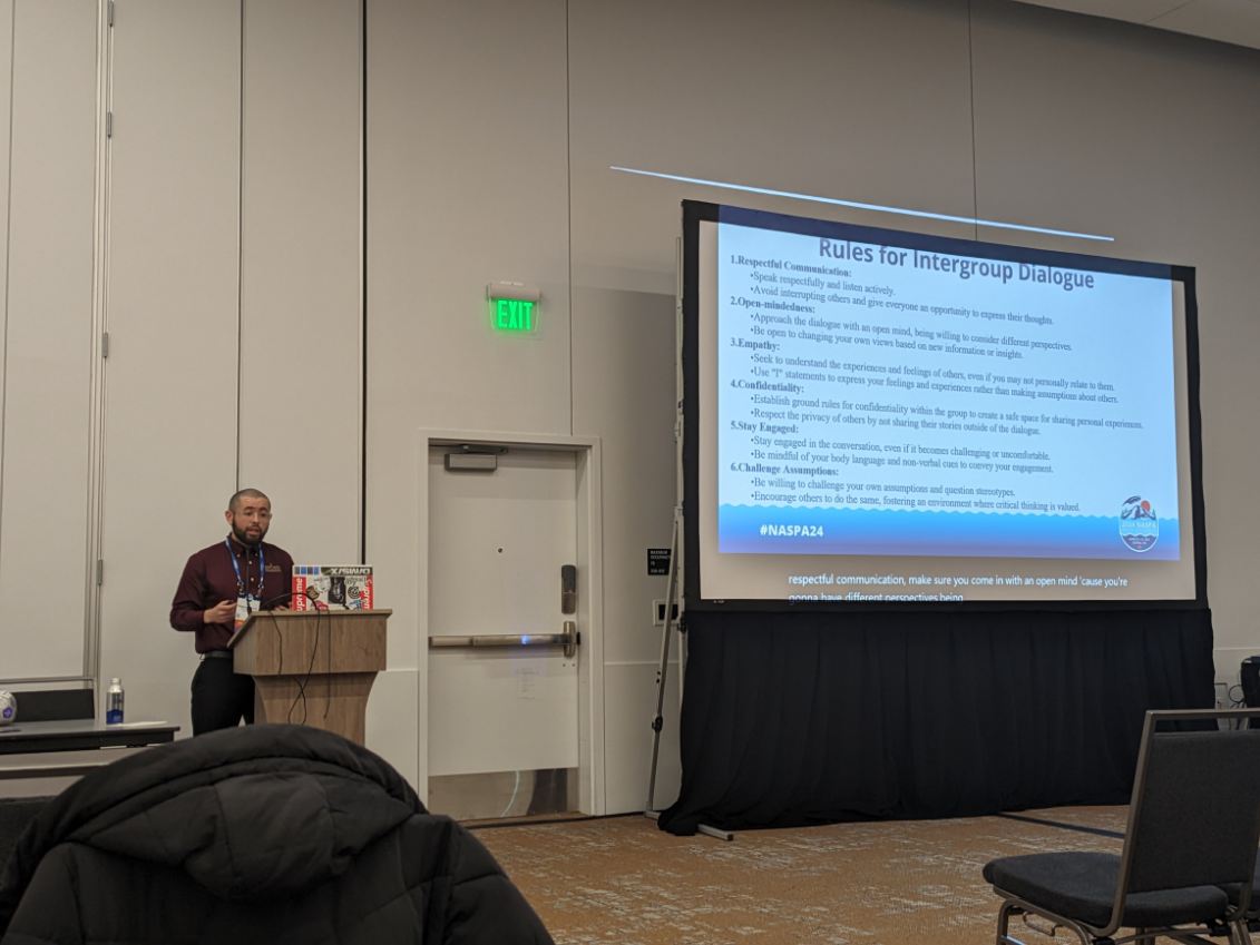 Male standing behind podium presenting research on a large projection screen