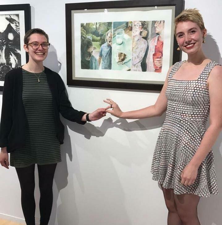Two female students smiling in front of a piece in the eckhaus gallery