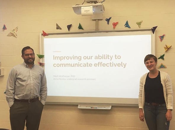 Dr. Wolfmeyer and KU student Anna Nissley, standing on either side of a powerpoint slide that reads "improving our ability to communicate affectively"