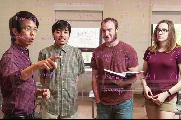 Dr. Tony Wong lecturing to three students on mathematics, with mathematic symbols written on glass board in the foreground