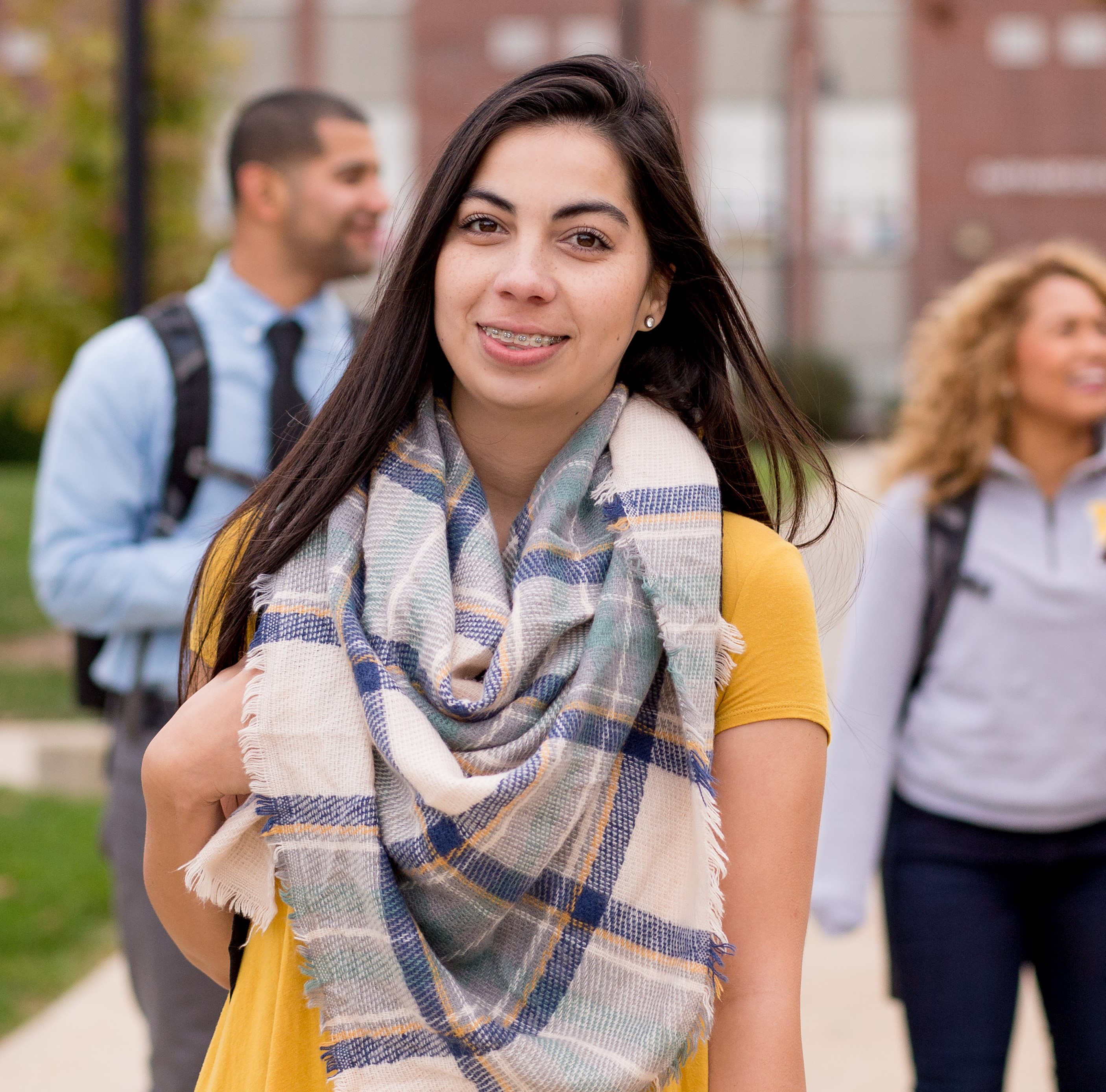 Female students smiling while walking on a path in front of Old Main, with other students also walking on the same path in the background