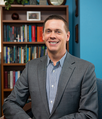 Image of Dr. Matthew Wintersteen in front of bookcase and blue background