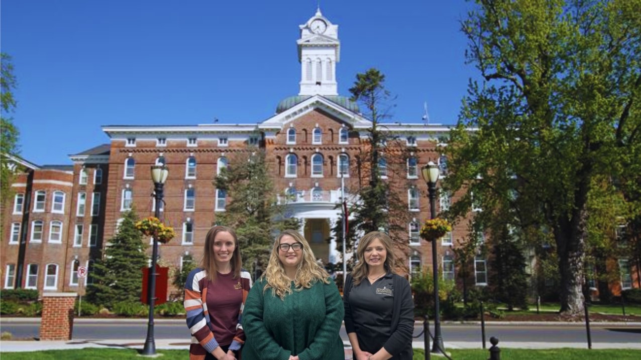 Three women standing in front of Old Main University at Kutztown University of Pennsylvania with trees in background
