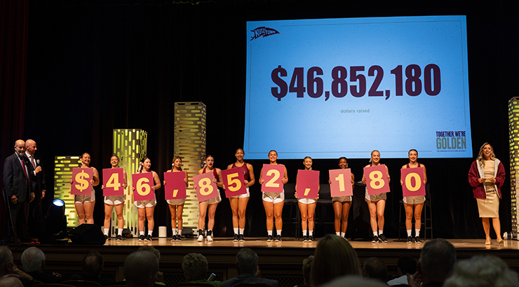 Cheerleaders on stage, showing amount of dollars raised.