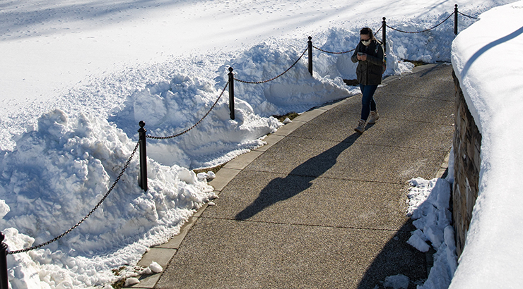 Student walking on sidewalk with snow off to side
