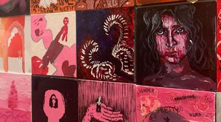 Wall decorated with various paintings, including one of a woman whose face is dripping with blood and one of red stick figures arguing over pink mist 