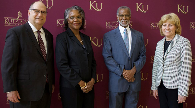 Speakers at press conference in front of KU backdrop.