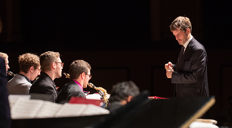 Conductor in front of jazz ensemble in black suit.