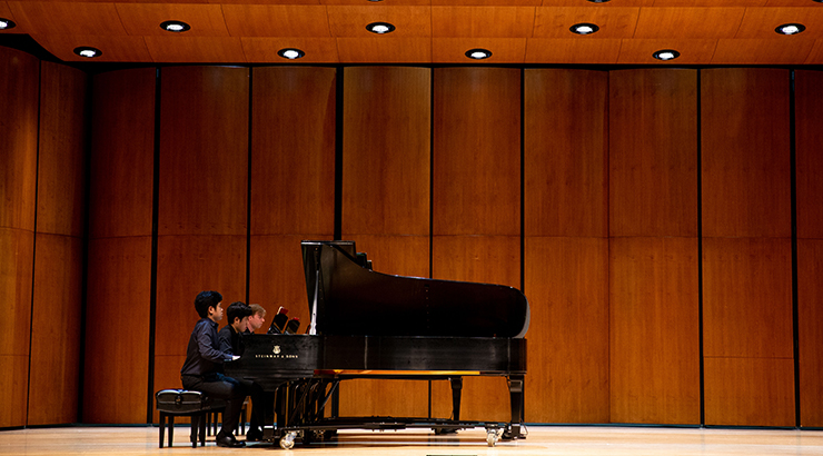 Students playing piano on stage.
