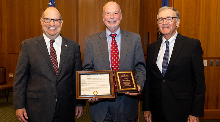 Trustee Ludlow posing with two award plaques.