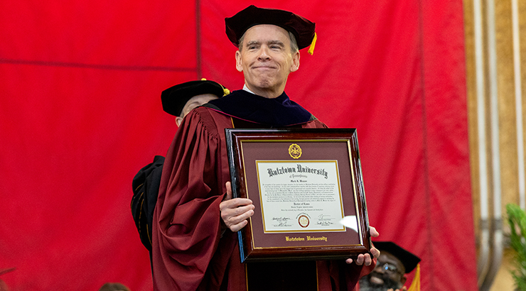Weaver holding diploma frame on stage