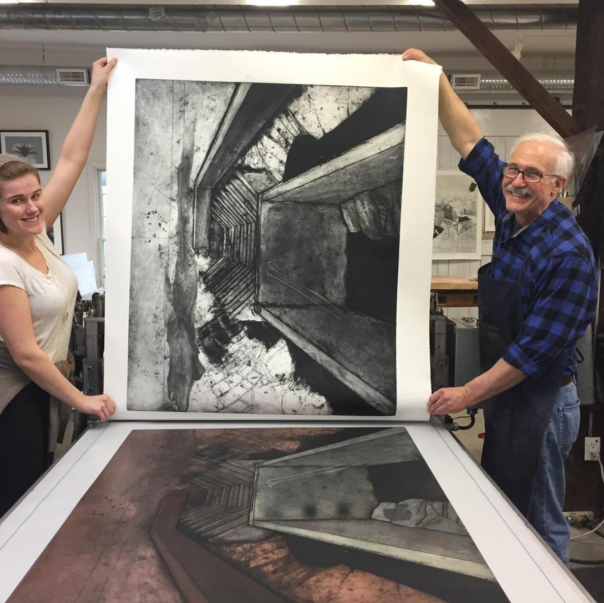 Instructor and student smiling as they hold up a freshly finished black and white print of abstract layers with varying patterns