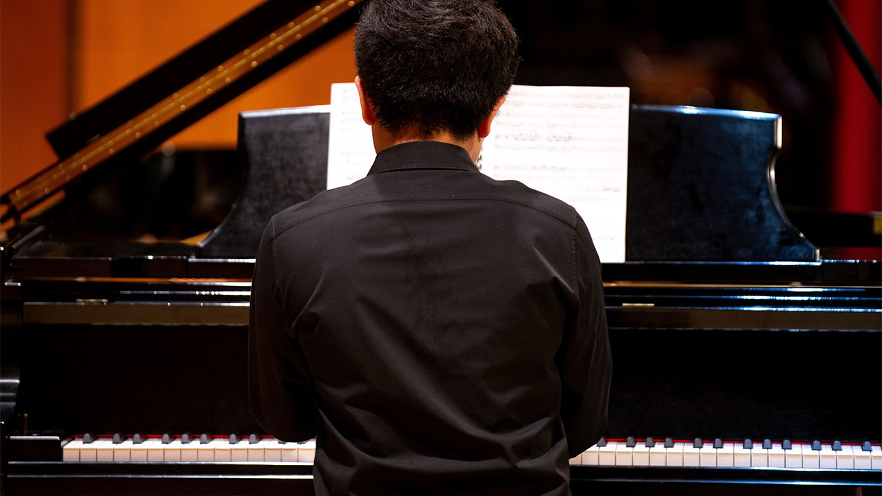 Student with their back to the camera playing a song on a grand piano