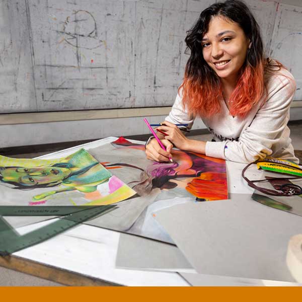 A female art student seated at a desk working on art work