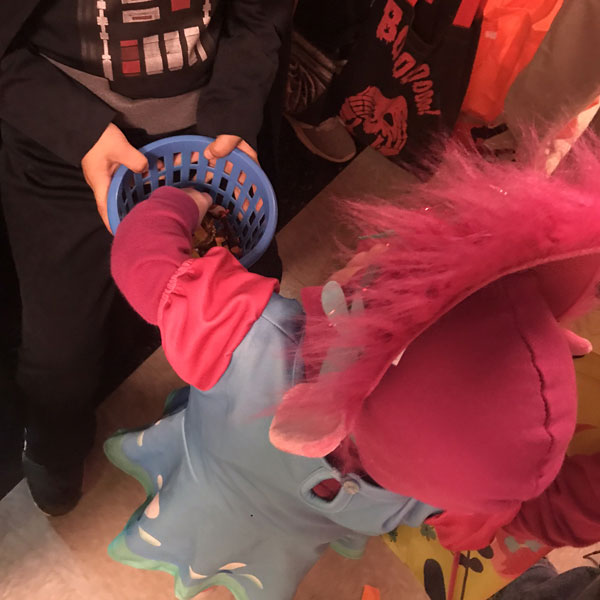 Child in Halloween costume taking candy from student's treat basket at HARLOween