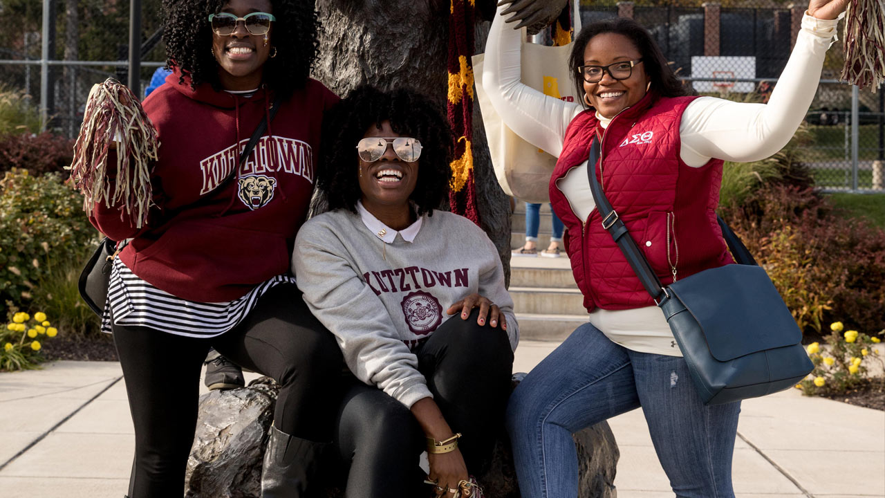 Three Female African Americans demonstrating KU pride by posing together wearing all KU clothing and waving spirit pom poms