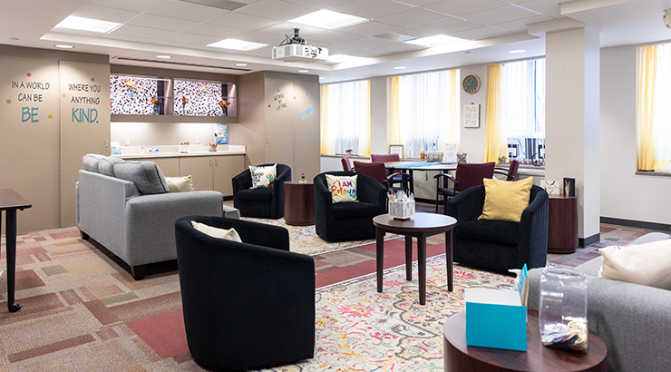 Health Center facility. with signs that read "In a world where you can be anything, be kind." couches and chairs with colorful pillows adorn the room.