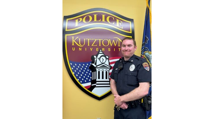 Buckley standing in front of KU Police badge on wall, with flag to the side