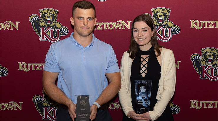 Kutztown University students holding trophies in front of maroon backdrop
