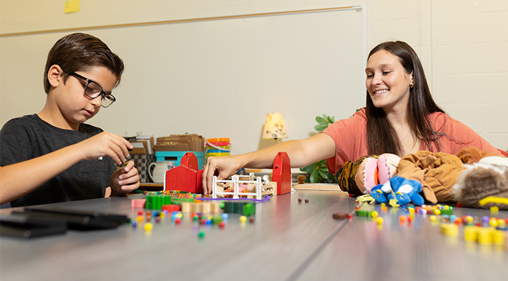 Early childhood education major working with student on a puzzle in classroom.