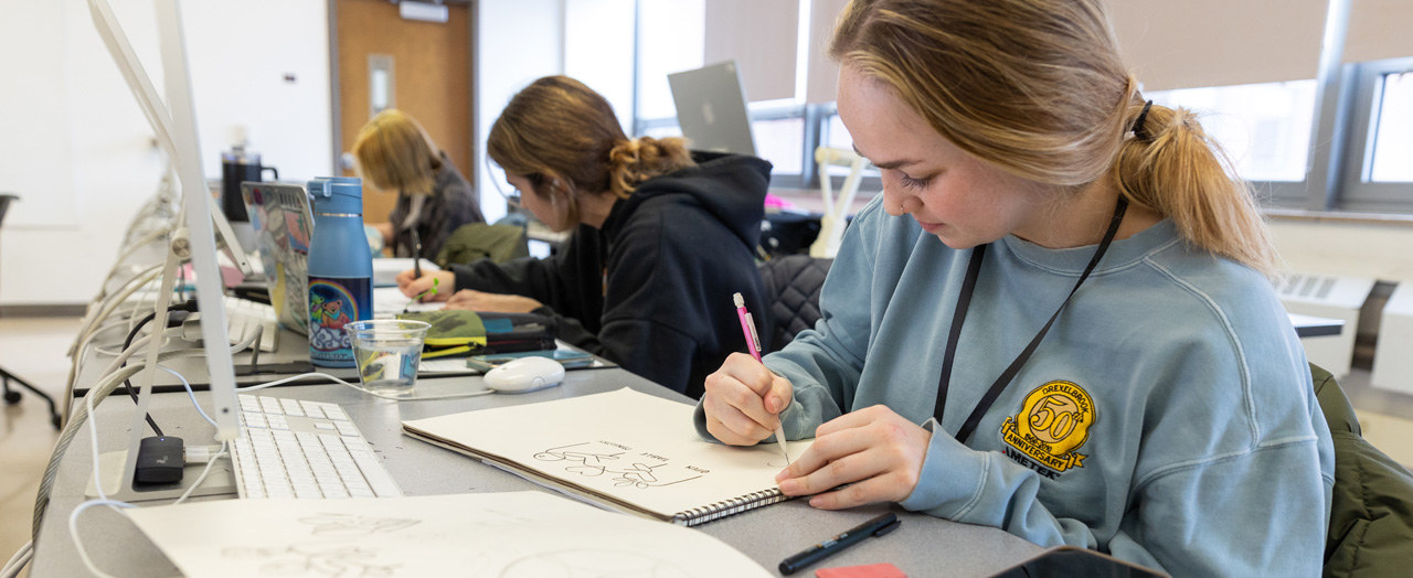 a group of three female students at a desk working on designs