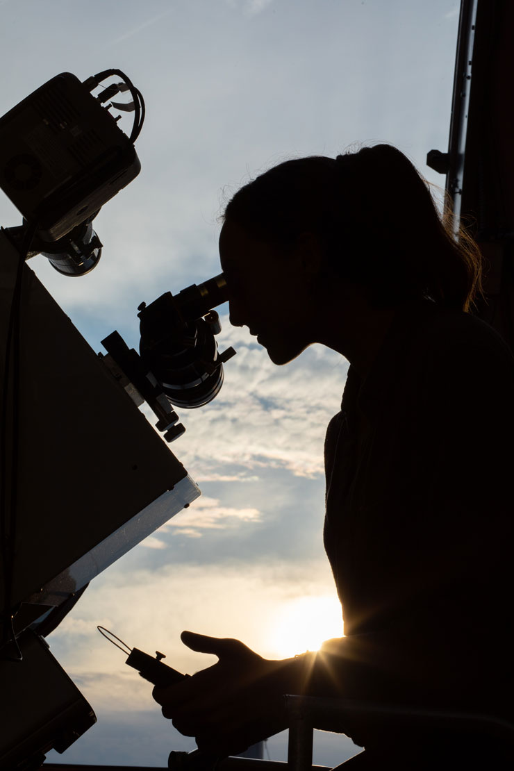 silhouette of student looking into the telescope at Kutztown's Chambliss Observatory, as clouds and a sunny sky are visible in the distance.