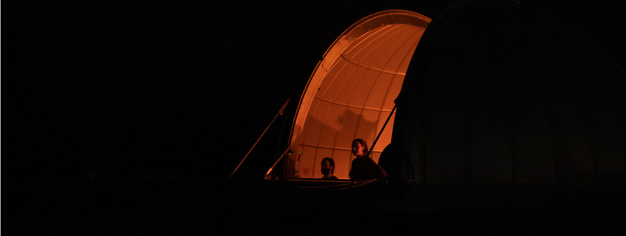 night time look into the opening of Kutztown University's Chambliss Observatory, as two individuals look out of the opening.