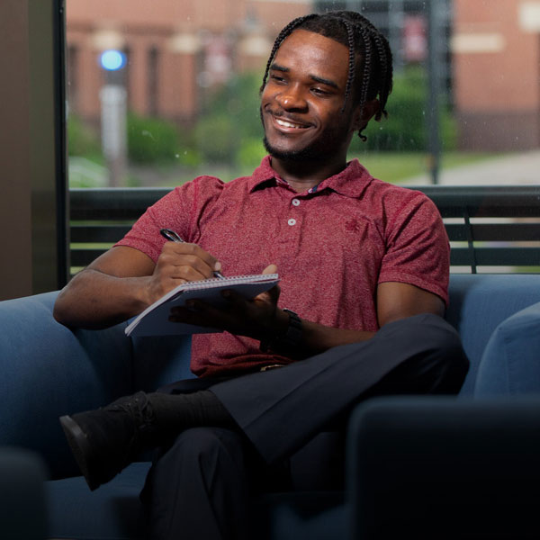 Male business administration marketing majorsmiling while holding a pen and notepad.