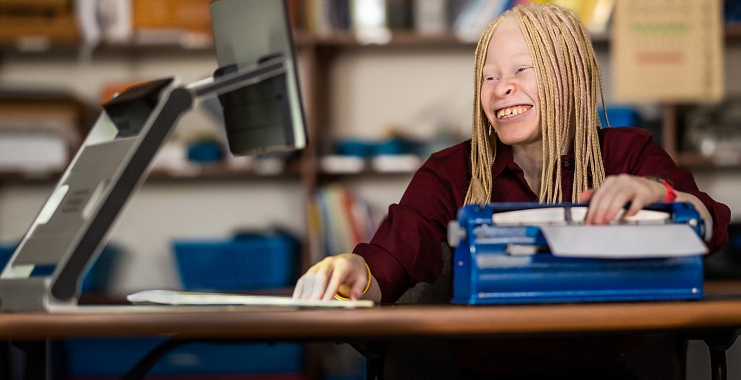 Smiling female student, working with braille machine and computer