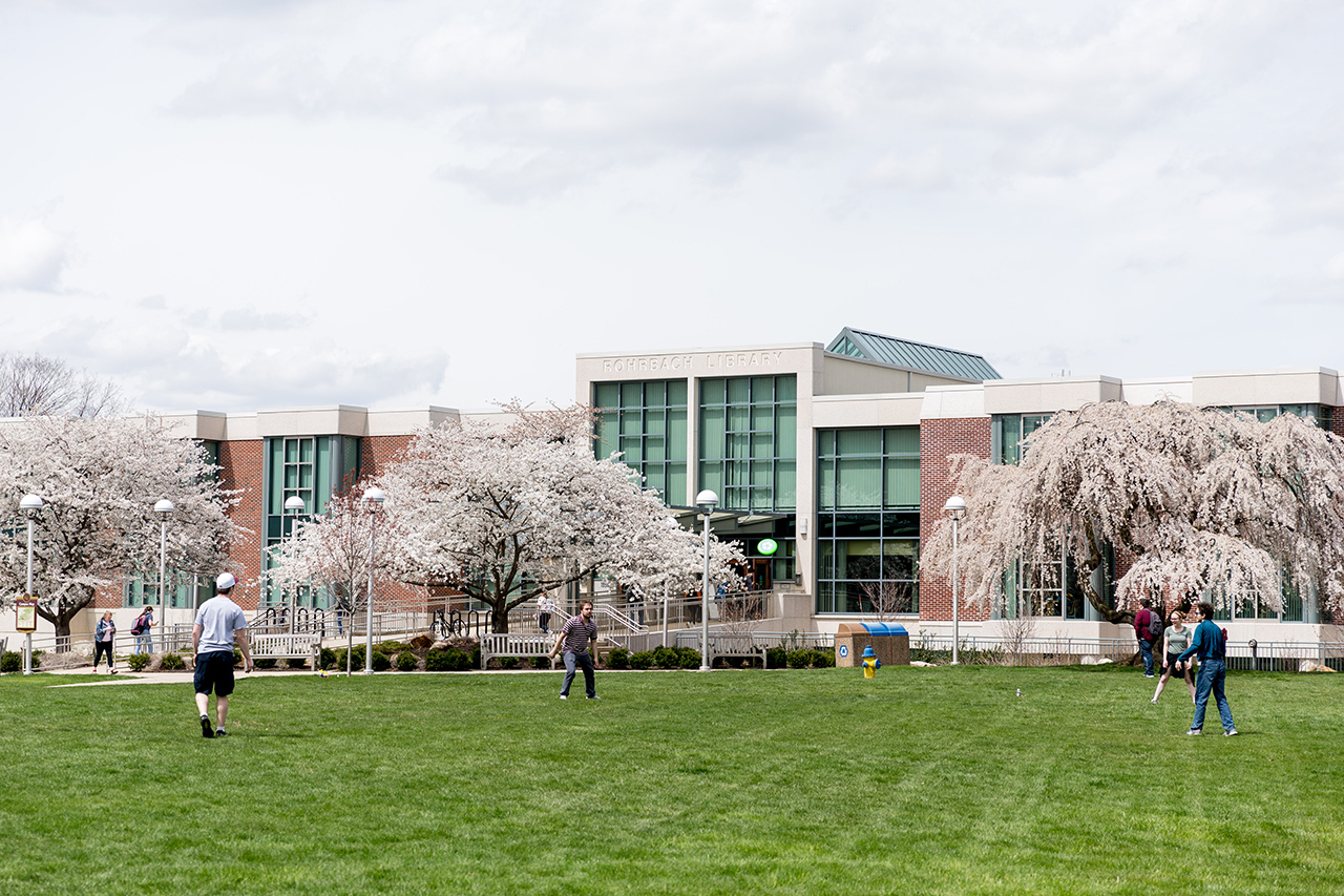 Rohrbach Libary with flowering trees and students playing a game in the foreground