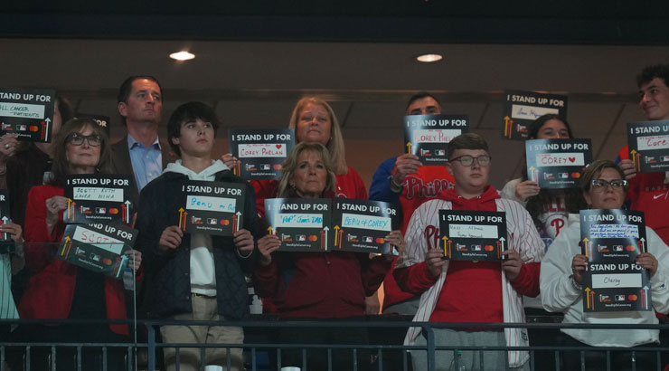 First Lady Jill Biden, middle front, with Luke Theodosiades, front, second from right, along with others all holding Stand Up to Cancer signs.