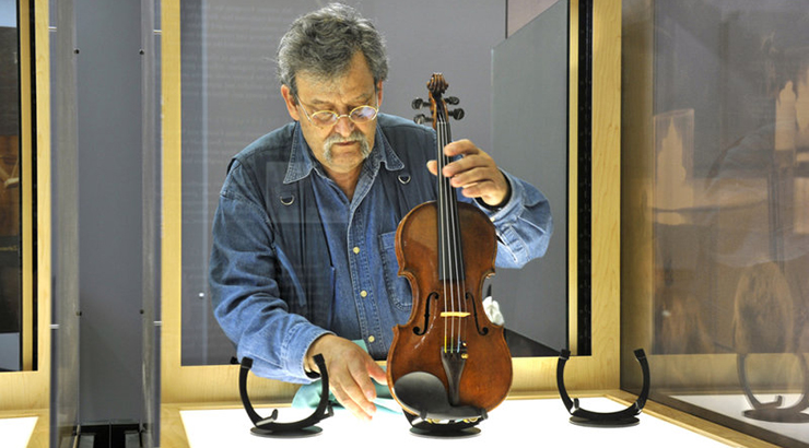 Man placing a violin on a stand in a glass case