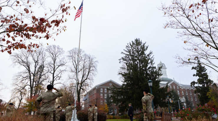 members of the KU student veterans and ROTC salute the flag as it is raised with Old Main clock tower in the background.