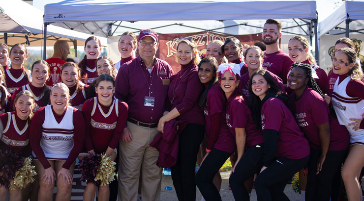 cheerleaders and others dressed in maroon KU spirit gear pose with President and Mrs. Hawkinson at homecoming 2023.