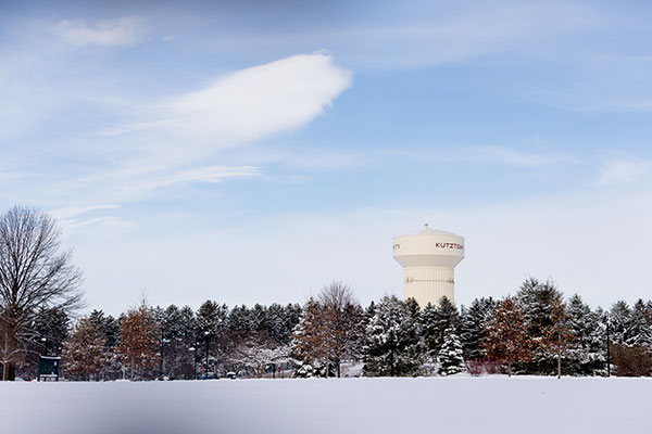 a pristine field on untouched snow framed by pine trees lightly covered in snow and the KU water tower against a blue sky