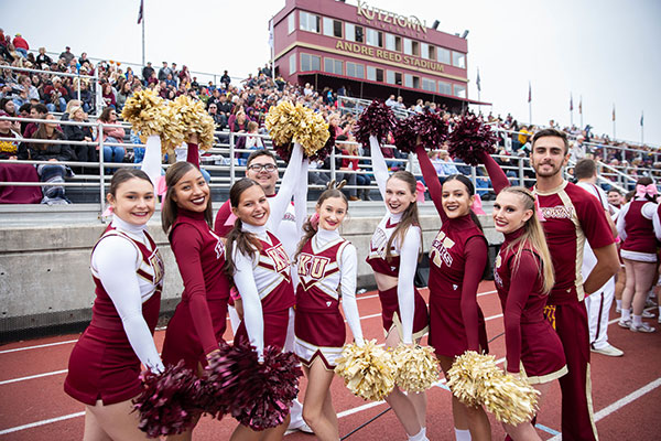 A group of male and female cheer leaders pose on the track in front of stands full of fans in Andre Reed Stadium.