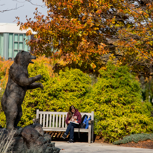 student sitting next to bear statue with fall trees