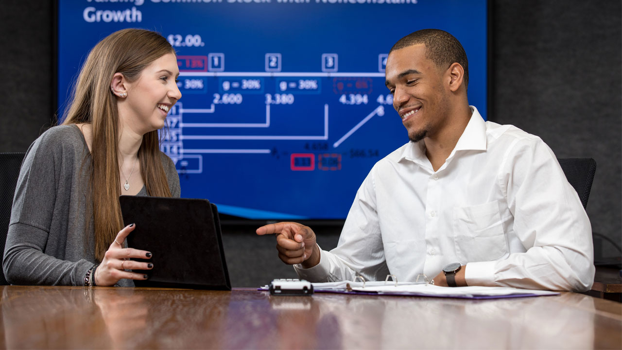 Female and male students working with a tablet, in front of a visual of a business chart