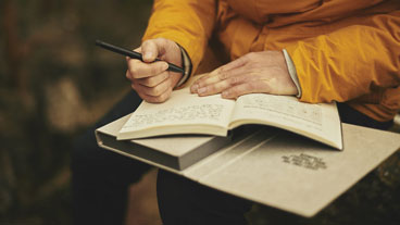 close up view of writer in a yellow jacket with pen in hand, writing in a book.