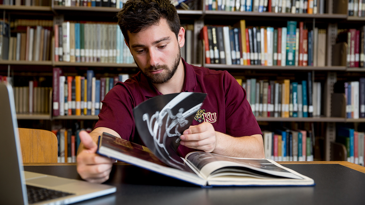 student flipping through book sitting in library
