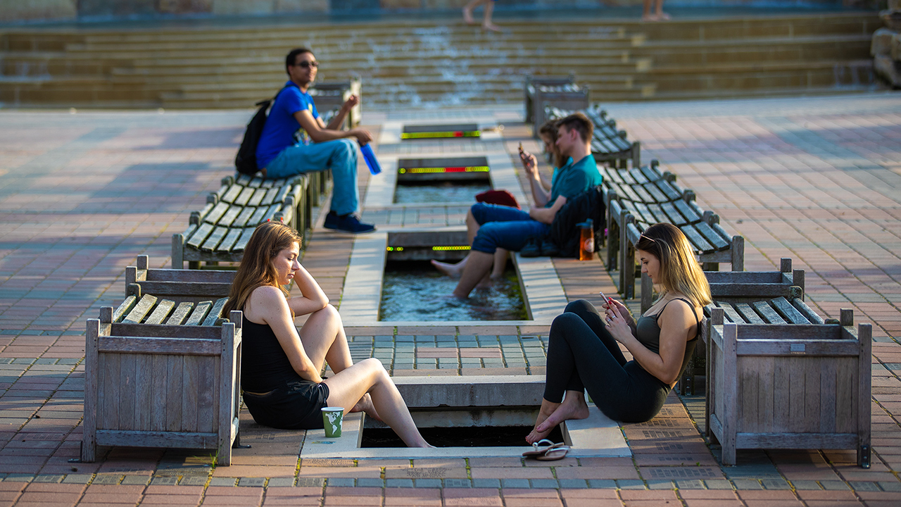 group of students on their phones relaxing at the alumni plaza