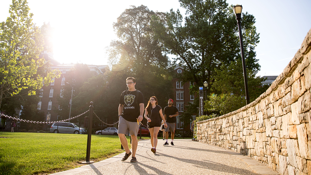 students walking towards the alumni plaza with the sun glaring in the background