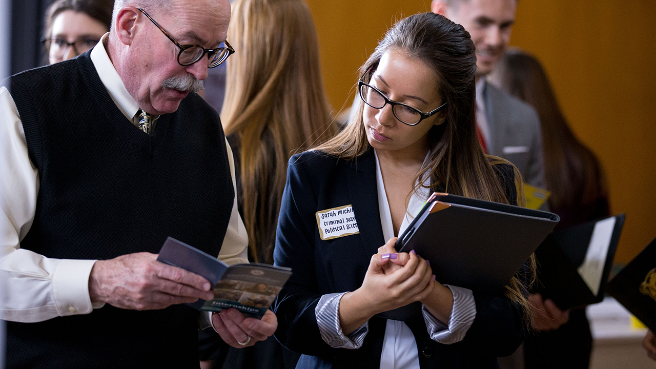 female student holding binder looking at brochure with older male