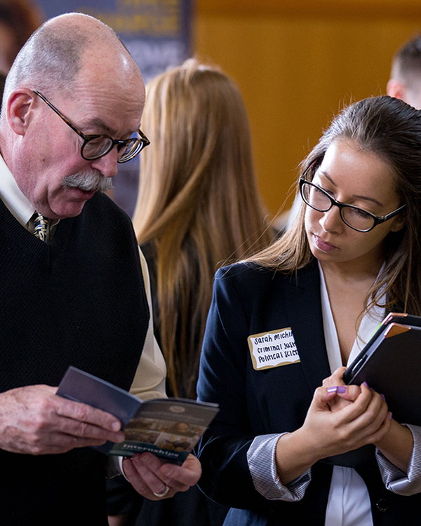 female student holding binder looking at brochure with older male