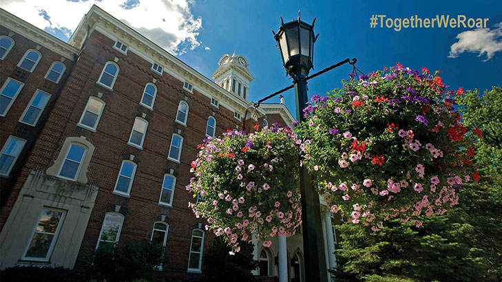 Looking up at the old main clock tower with blue skies and the familiar light post with summer hanging floral baskets